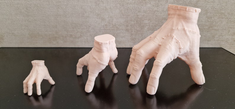 Op de afbeelding: Drie verschillende maten, lichtroze, 3D-geprinte handen met elk vier vingers. De handen zijn geposeerd alsof ze op handen en voeten lopen.