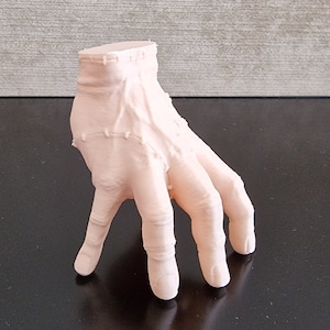 Op de afbeelding: Een 3D-geprint model van een menselijke hand met alle vingers gestrekt. De hand is gemaakt van lichtroze plastic en is geposeerd alsof hij reikt.
