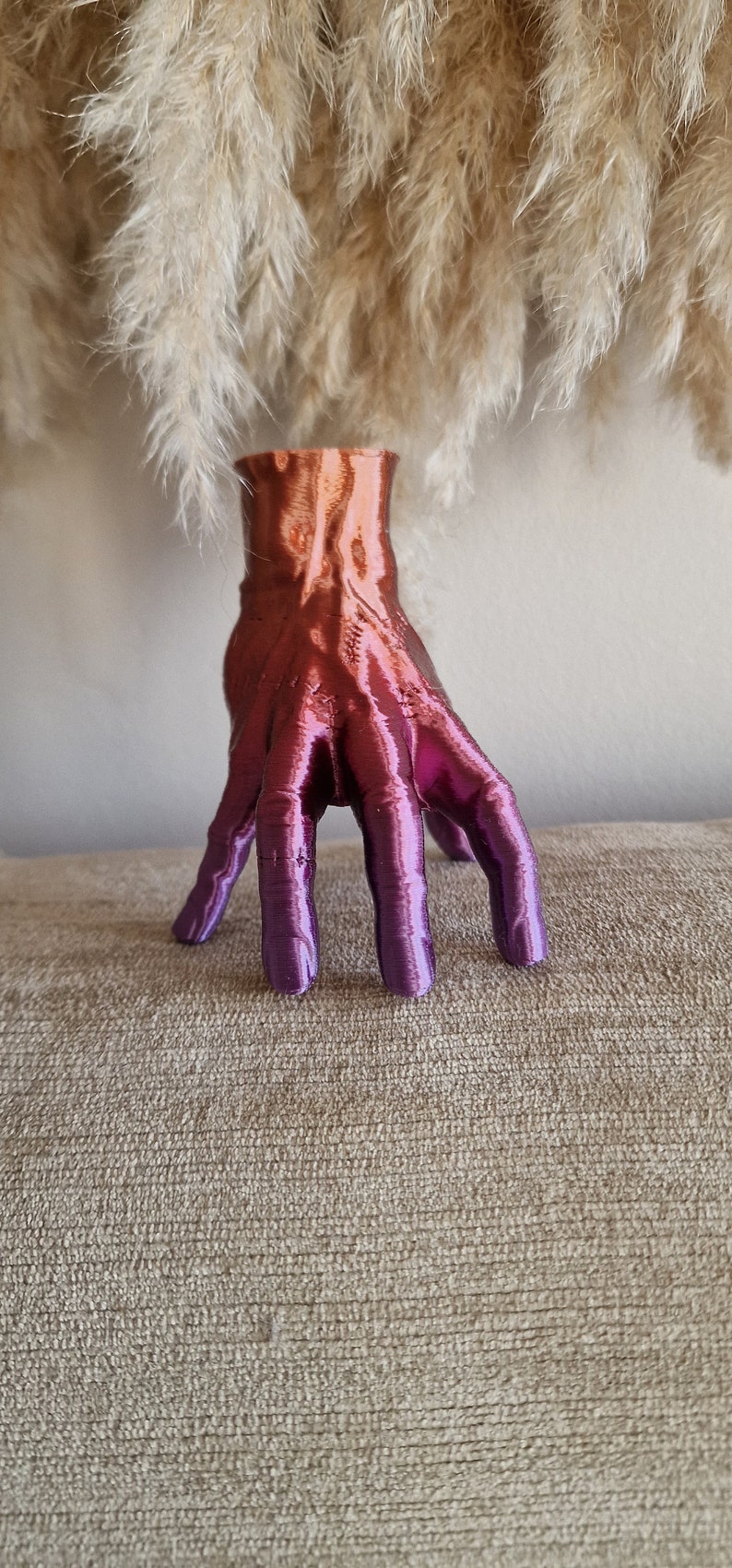 Op de afbeelding: Een handvormige vaas met een kleurverloop van oranje naar paars. De vaas is gemaakt van een glad, glanzend materiaal en heeft een uniek, abstract ontwerp.