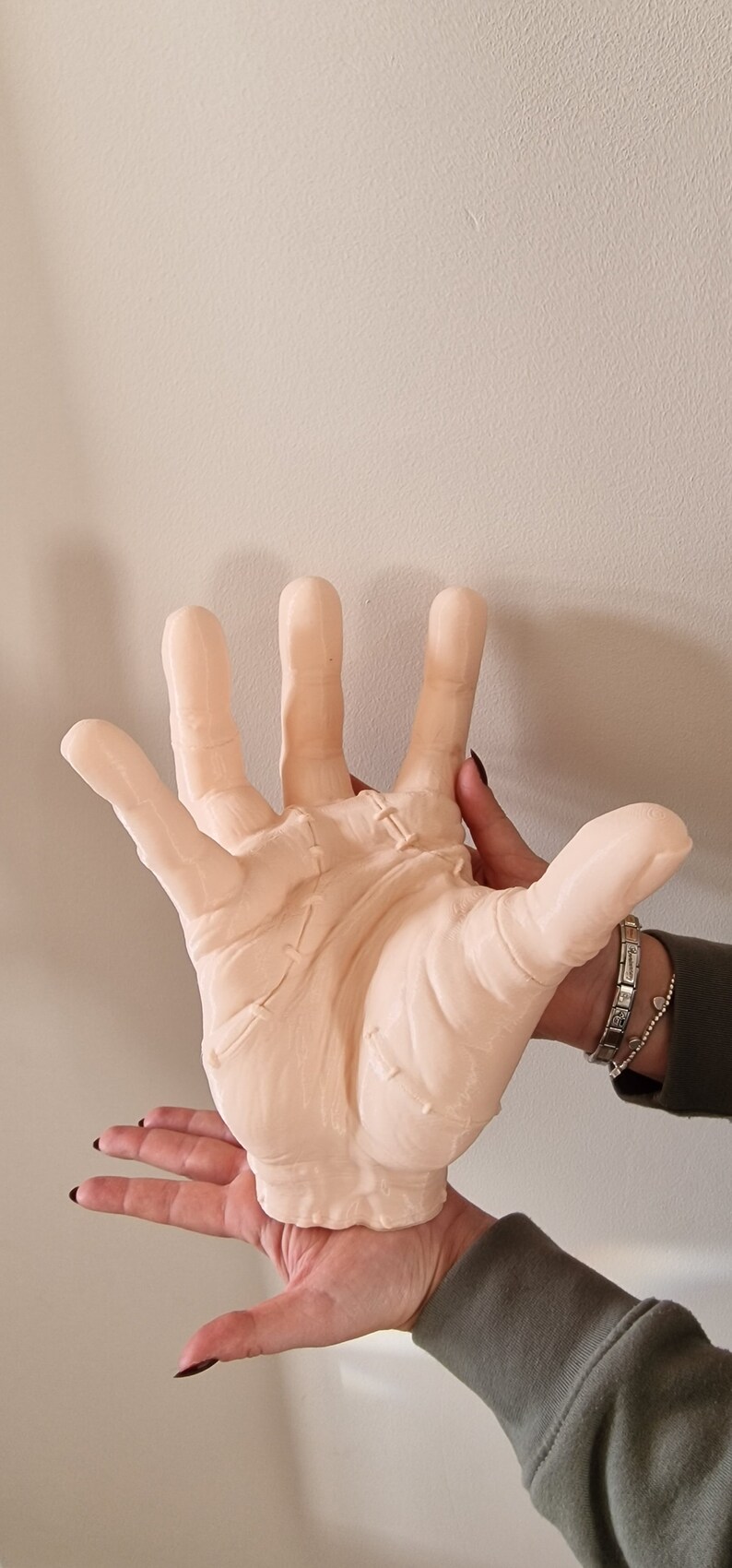 Op de afbeelding: Een groot, lichtroze, gedetailleerd, realistisch handbeeld met gestikte naden. De hand wordt vastgehouden door een hand van een persoon.