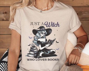 May include: A beige t-shirt with a graphic of a witch reading a book. The text on the shirt reads "Just a Witch who loves books".
