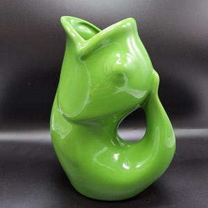 May include: A glossy, lime green ceramic vase with an organic, flowing design. The vase features a large opening and a unique, asymmetrical shape, with a hole in the side. The smooth surface reflects light, highlighting its curves.