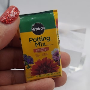 Pode incluir: Um saco em miniatura de Miracle-Gro Potting Mix. O saco &eacute; amarelo e verde, com o nome da marca e do produto em destaque. O saco apresenta imagens de flores coloridas e o texto "Grow Plants Twice As Big!"