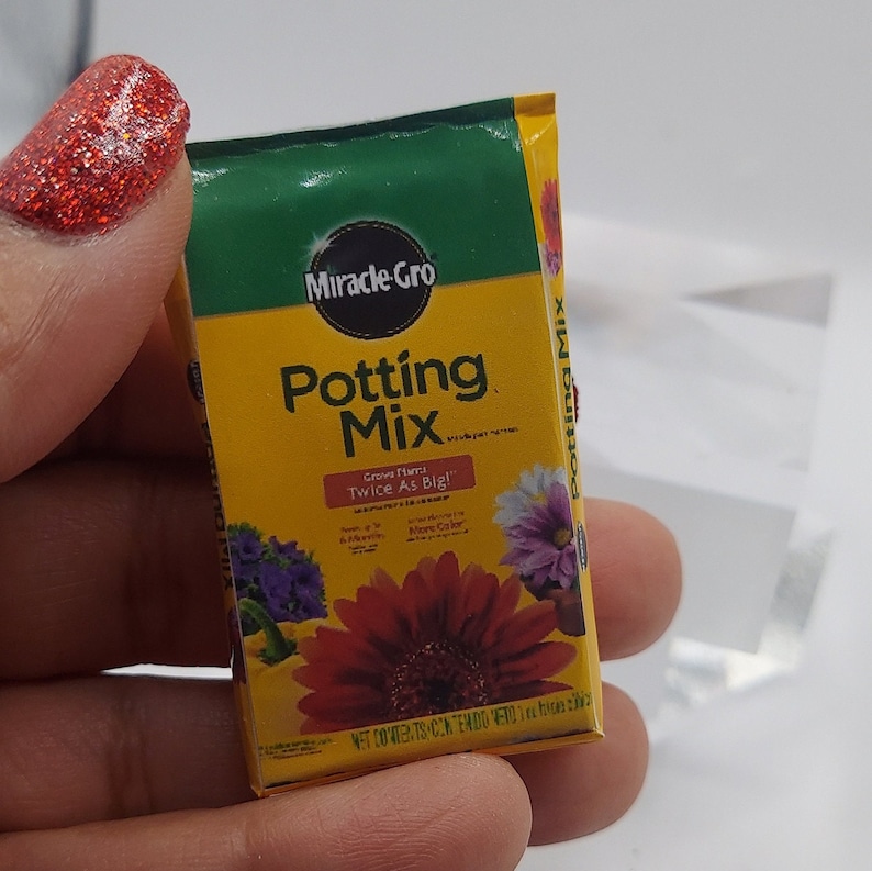 Pode incluir: Um saco em miniatura de Miracle-Gro Potting Mix. O saco &eacute; amarelo e verde, com o nome da marca e do produto em destaque. O saco apresenta imagens de flores coloridas e o texto "Grow Plants Twice As Big!"