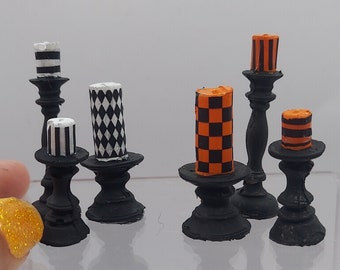 May include: Five black candle holders with various black and white, and orange and black patterned candles. The candles are on a white surface.