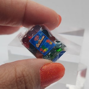 Könnte beinhalten: Eine kleine Packung bunter, runder Bonbons, verpackt in durchsichtigem Plastik. Die Packung hat ein blaues Etikett mit dem Text "Gel Snacks" und einem Bild von Früchten.