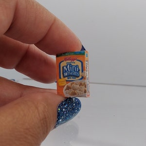 May include: A miniature box of Kellogg's Frosted Mini-Wheats cereal. The box is blue and yellow with the product name and logo printed on the front.