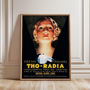 May include: Framed vintage advertisement for Tho-Radia beauty products. The poster features a woman's face lit from below, with yellow and white text. The product name is prominent, along with French text. A classic art deco style.