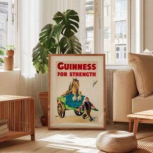 K&ouml;nnte beinhalten: Ein gerahmtes Vintage-Guinness-Poster. Das Kunstwerk zeigt einen pferdegezogenen Wagen mit einem Mann, der daneben l&auml;uft. Der Text "Guinness For Strength" ist rot. Das Poster befindet sich in einem Holzrahmen und wird in einem hellen Raum ausgestellt.