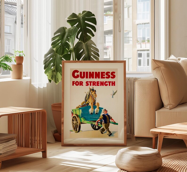 K&ouml;nnte beinhalten: Ein gerahmtes Vintage-Guinness-Poster. Das Kunstwerk zeigt einen pferdegezogenen Wagen mit einem Mann, der daneben l&auml;uft. Der Text "Guinness For Strength" ist rot. Das Poster befindet sich in einem Holzrahmen und wird in einem hellen Raum ausgestellt.