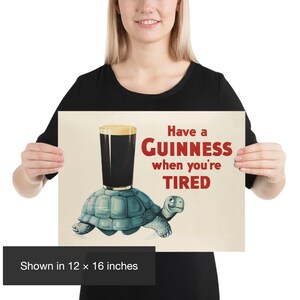K&ouml;nnte beinhalten: Ein Poster mit dem Text "Have a Guinness when you're TIRED". Das Bild zeigt ein Pint Guinness, das auf einer blauen Schildkr&ouml;te balanciert. Das Poster wird in 30,48 x 40,64 cm angezeigt.