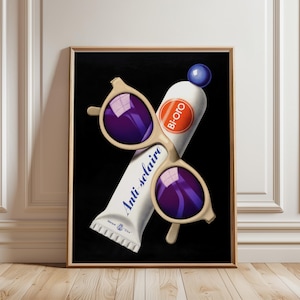 May include: A framed art print depicting a tube of sunscreen and sunglasses against a black background. The sunglasses have a light beige frame and purple lenses. The sunscreen tube is white with the words "Anti-solaire" and "Bi-Oro". A blue sphere is on top.