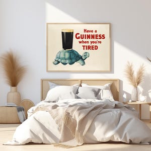 K&ouml;nnte beinhalten: Gerahmter Druck mit einem Cartoon-Schildkr&ouml;te, die ein Guinness-Bier tr&auml;gt. Der Text lautet: &bdquo;Have a Guinness when you're TIRED&ldquo; in Rot und Schwarz. Das Kunstwerk hat eine Vintage-&Auml;sthetik im Pub-Stil.