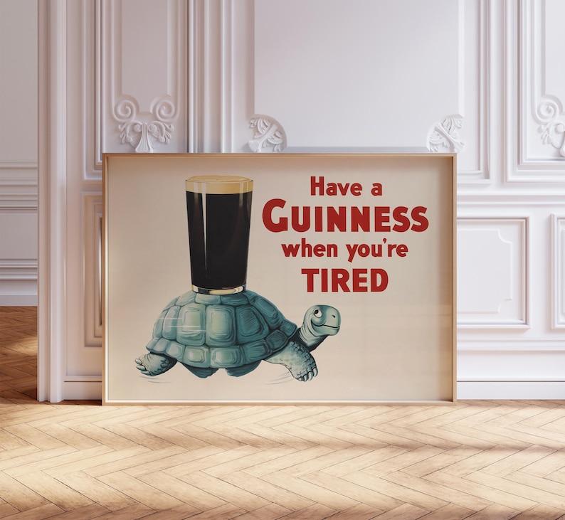 K&ouml;nnte beinhalten: Ein gerahmter Druck mit einem Guinness-Pint auf einer t&uuml;rkisfarbenen Schildkr&ouml;te. Der rote Text lautet "Have a Guinness when you're TIRED". Das Bild hat einen Vintage-Cartoon-Stil.