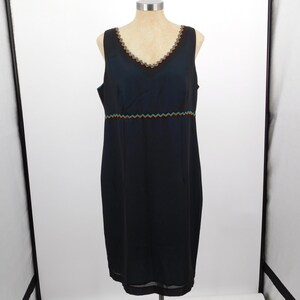 May include: Black sleeveless dress with a V-neckline and a knee-length hem. The dress features a colorful zigzag trim along the neckline and waist. The dress is displayed on a mannequin.