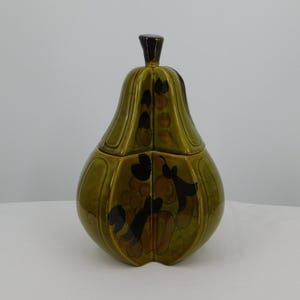 May include: A green ceramic pear-shaped jar with a lid and a dark brown knob. The jar has a glossy finish and is decorated with black and brown floral designs. The jar is likely used for storage.