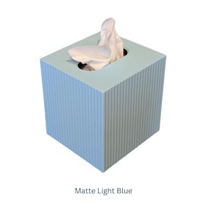 May include: A light blue tissue box with a ribbed texture. The box has a square shape and a white tissue is partially visible.