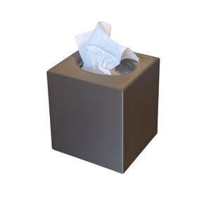 May include: A square, dark gray tissue box with a circular opening at the top. White tissues are pulled from the opening, creating a contrast with the box's solid color. The box is a simple, modern design.