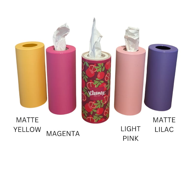 May include: Four tissue box holders in different colours: matte yellow, magenta, light pink, and matte lilac. The holder in the centre has a pomegranate pattern and the text "Kleenex" on it.