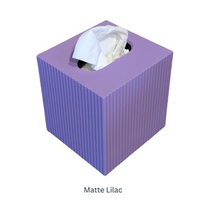 May include: A matte lilac tissue box cover with a ribbed texture. The cover has a square shape and a rectangular opening for tissues.