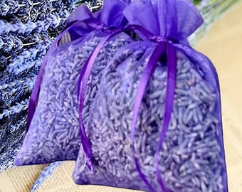 May include: Two purple mesh sachets filled with dried lavender buds, tied with matching ribbon. The sachets are in front of a backdrop of lavender sprigs. The image has a soft focus, highlighting the natural texture and color of the lavender.