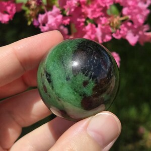 May include: A green and black gemstone sphere, polished to a smooth finish. The sphere is about the size of a golf ball and has a swirling pattern of green and black.