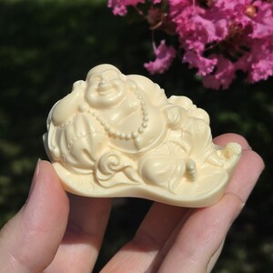 May include: A small, white, carved figurine of a smiling Buddha sitting on a cloud. The figurine is made of a smooth, ivory-like material.