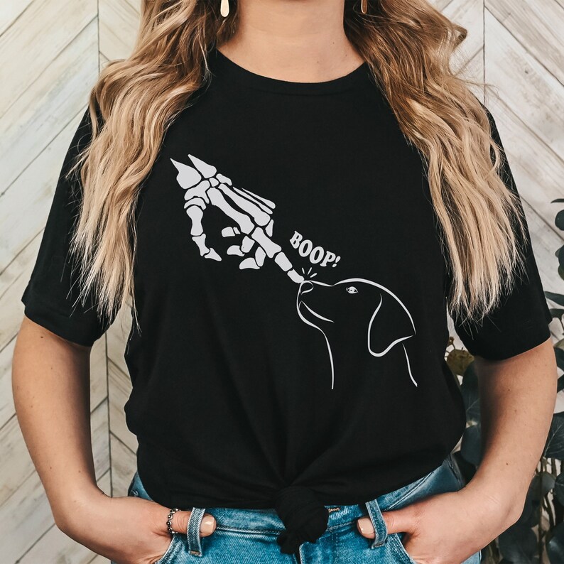 May include: Black t-shirt featuring a white skeleton hand booping a dog's nose. The text "BOOP!" is above the dog's nose.