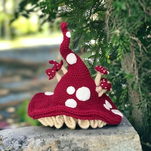 May include: A crocheted mushroom house with a red hat and white spots. The house has several smaller mushrooms growing from the base.