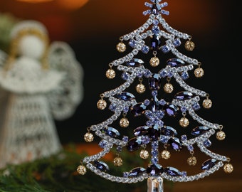 Puede incluir: Un pequeño adorno de árbol de Navidad decorativo, de color morado y dorado, con joyas. El árbol está hecho de metal y tiene un soporte.