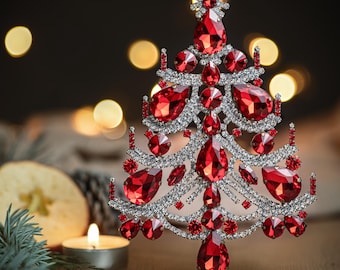 May include: A red jeweled Christmas tree ornament with a silver base. The ornament is made of rhinestones and red glass beads.