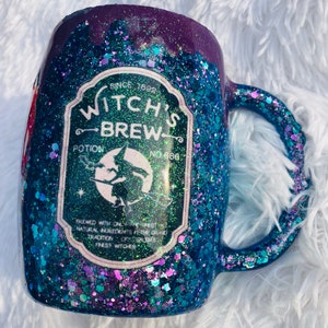 May include: A teal and purple glitter mug with a white label that reads "Witch's Brew Potion No. 666" and a witch flying on a broomstick. The label also says "Brewed with only the finest natural ingredients from the grand tradition of Salem's finest witches."