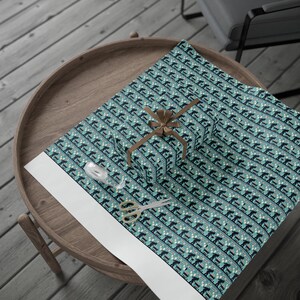 May include: A wrapped gift with a brown ribbon sits on patterned wrapping paper. The paper features a repeating pattern of skiers in navy blue and white on a teal background. Scissors and tape are also on the wooden table.