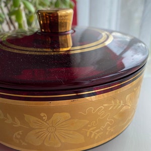 May include: A vintage glass trinket box with a red base and gold accents. The lid has a gold trim and the base has a gold floral design.