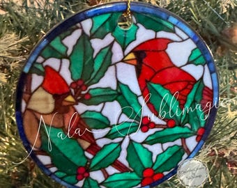 May include: A ceramic ornament featuring a stained-glass design with two red cardinals, green holly leaves, and red berries. The ornament is approximately 3 inches in diameter and has a blue border. The text "Cardinals and Holly Ceramic Ornament" is at the top.