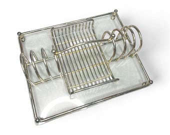 May include: A silver-toned metal desk organizer with a clear glass base. The organizer features a section for holding pens or pencils, a section for holding mail, and a section for holding notepads or small papers. The design is minimalist and modern.