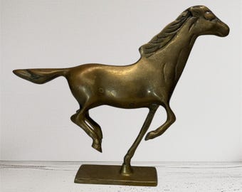 May include: A bronze-colored horse sculpture in a running pose. The horse is mounted on a rectangular base. The sculpture has detailed features, including a flowing mane and tail. The horse is depicted mid-stride, with its legs extended.