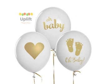 May include: Three white balloons with gold lettering. The balloons have the phrases "oh baby", "Oh Baby!" and a heart.