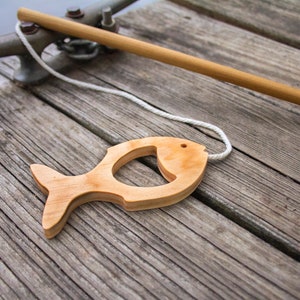 May include: A wooden fish toy with a string attached to it. The fish is lying on a wooden dock.