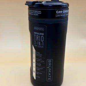 Op de afbeelding: Zwarte BRUMATE Hopsulator Trio 3-in-1 blikjeskoeler en tumbler. Voorzien van een lekvrij deksel, een Push-Lock pakking en een vaatwasmachinebestendig ontwerp. Geschikt voor 473 ml blikjes. De tekst luidt "CAN COOLER LEAK-PROOF TUMBLER ALL-IN-ONE."
