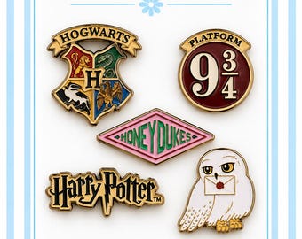May include: A set of five metal needlepoint minders featuring Harry Potter themed designs: the Hogwarts crest, a Platform 9 3/4 sign, a pink Honeydukes diamond, the Harry Potter logo, and a white owl holding a letter with a red wax seal.