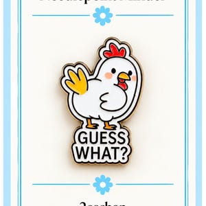 May include: A white enamel needlepoint minder pin featuring a cartoon chicken with a red comb, yellow wing, and orange feet. The chicken is positioned above a white speech bubble containing the black text GUESS WHAT? The pin has gold metal edges.
