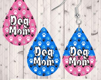 Könnte beinhalten: Tropfenförmige Ohrringe mit einem sich wiederholenden Pfotenabdruckmuster und dem Text Dog Mom. Ein Ohrring ist rosa mit weißen und schwarzen Pfotenabdrücken, der andere ist horizontal geteilt mit Blau oben und Rosa unten.