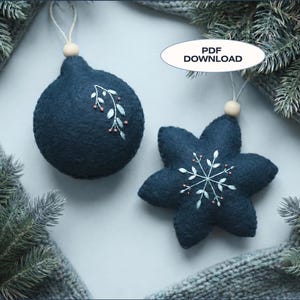 May include: Two navy blue felt Christmas ornaments. One is round with a floral design, the other is a star shape with a snowflake design. Both have a wooden bead and string for hanging. The text "PDF DOWNLOAD" is in the image.