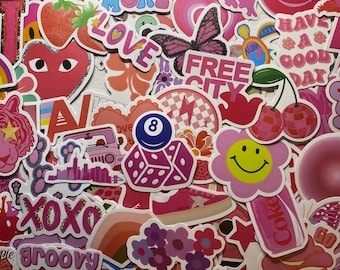 May include: A collection of pink and red stickers with various designs, including hearts, flowers, dice, a smiley face, a butterfly, and the words "XOXO", "groovy", "smile more", "love", "free city", "have a good day", and "aloha".