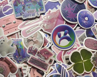 May include: A collection of colorful stickers featuring various designs, including a pink cassette tape, a pink phone, a green four-leaf clover, a purple and blue donut, a pink and white fan, a pink and white shoe, a purple and blue record, a pink and white computer, a pink and white car, a purple and blue rainbow, and the text "Trippy Gifs".