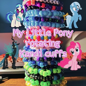 May include: A vertical stack of colorful plastic pony bead bracelets featuring letter beads that spell out names and phrases. The bracelets are decorated with My Little Pony character illustrations and star-shaped charms. The text My Little Pony rotating Kandi cuffs is overlaid on the image.