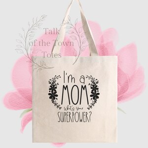May include: A white canvas tote bag with black text that reads "I'm a MOM What's your SUPERPOWER?" The text is surrounded by a wreath of black flowers.