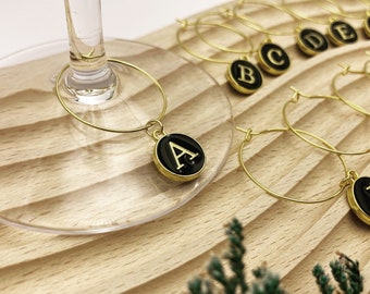 May include: Set of gold-toned wine glass charms with black typewriter key charms featuring the letters A through E.