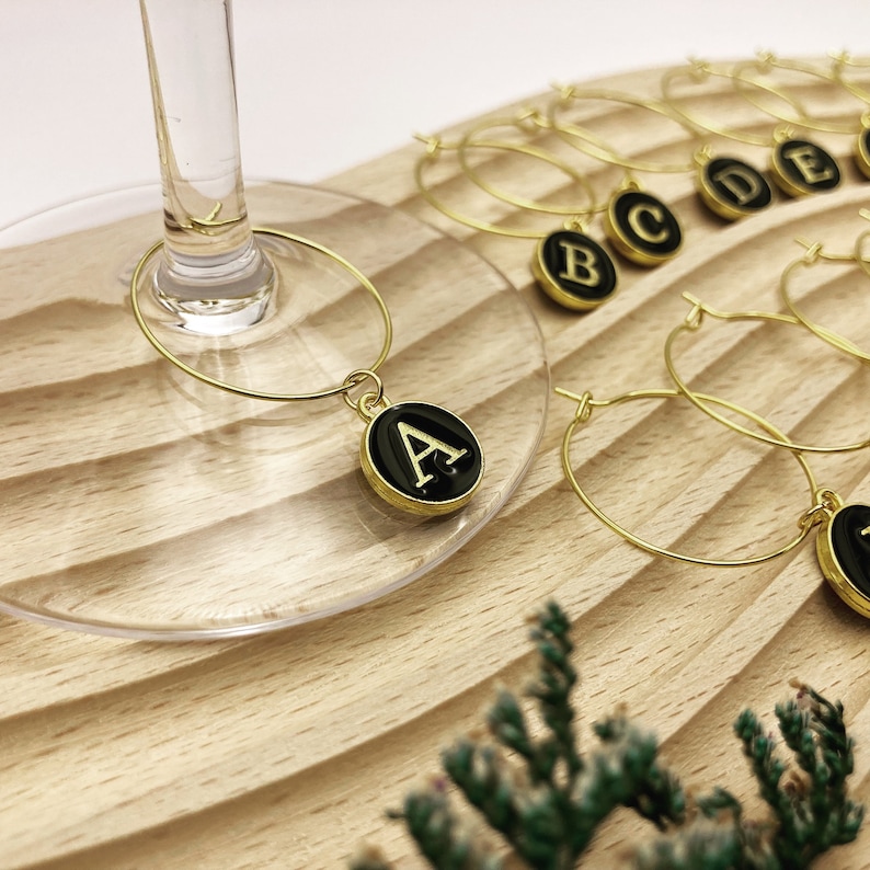 K&ouml;nnte beinhalten: Satz goldfarbener Weinglas-Anh&auml;nger mit schwarzen Schreibmaschinentasten-Anh&auml;ngern mit den Buchstaben A bis E.